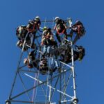 Technicians on cell tower against clear blue sky